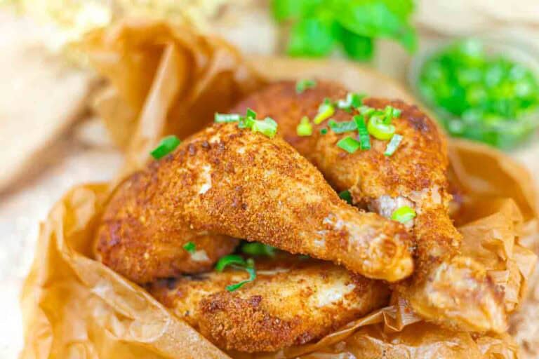 Two pieces of seasoned, breaded fried chicken garnished with chopped green onions on brown parchment paper.
