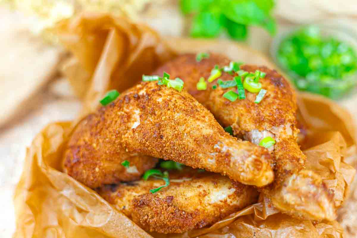 Two pieces of seasoned, breaded fried chicken garnished with chopped green onions on brown parchment paper.