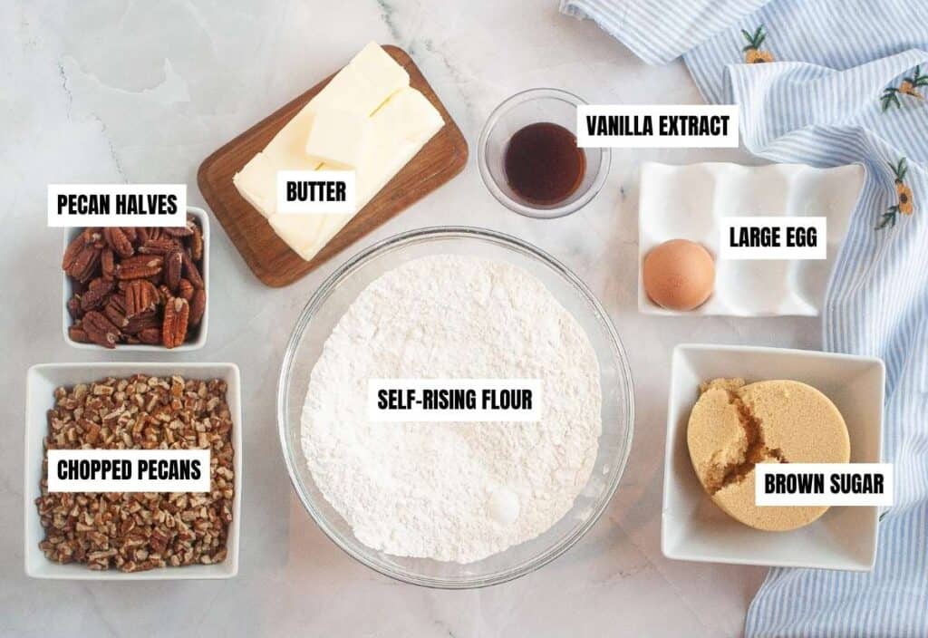 Flat lay of labeled butter pecan cookie ingredients including self-rising flour, brown sugar, butter, egg, vanilla, chopped pecans, and pecan halves.