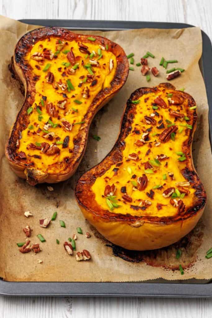 Close-up of roasted butternut squash halves filled with mashed squash and Parmesan, browned on top and garnished with chopped pecans and scallions.