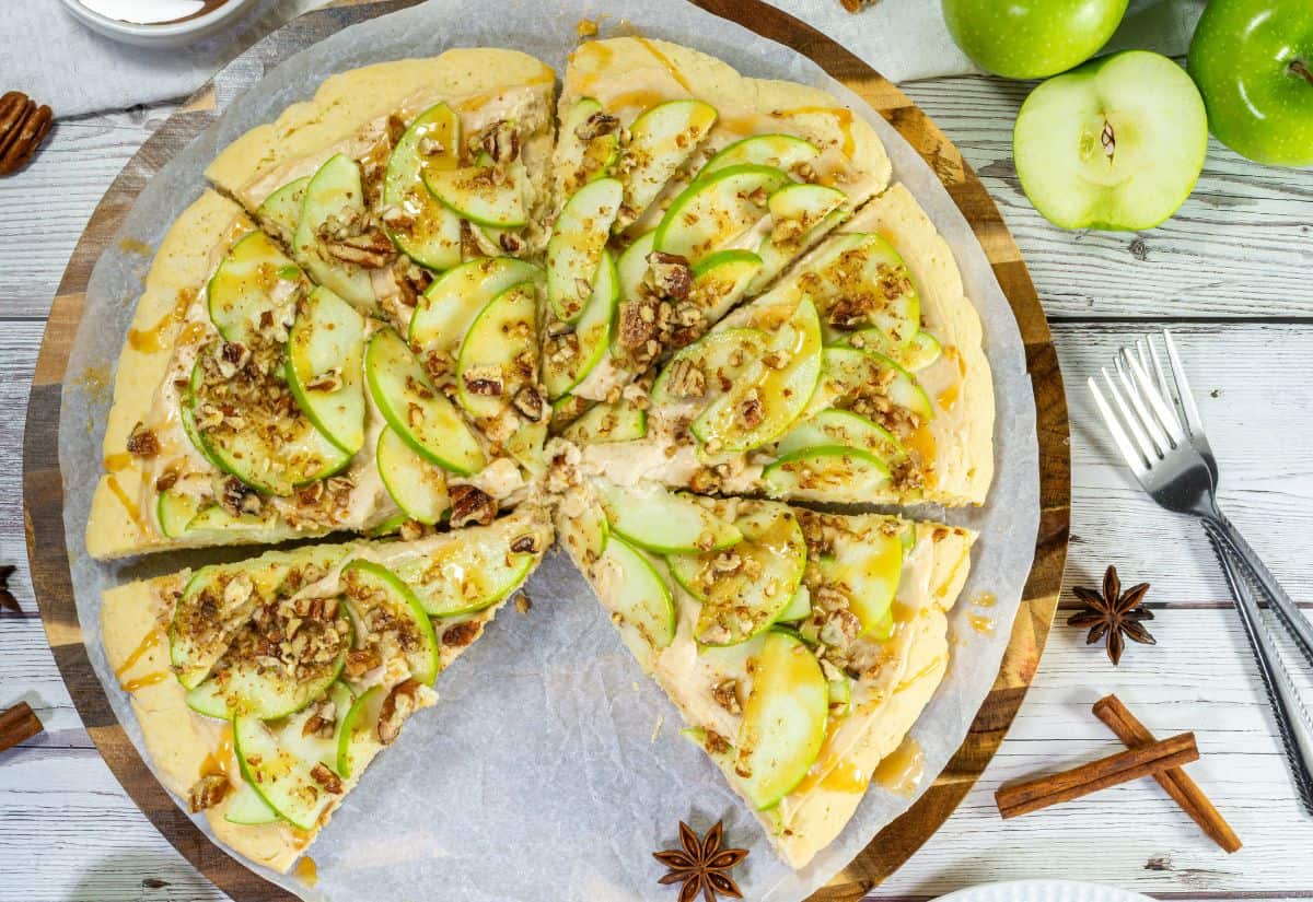 Sliced caramel apple pizza topped with Granny Smith apples, pecans, and caramel sauce, served on parchment paper.