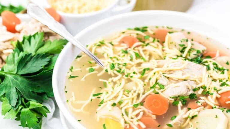 A bowl of chicken noodle soup with carrots, herbs, and noodles in a clear broth.