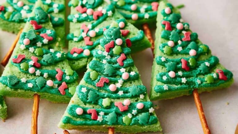 Green frosted sugar cookies shaped like Christmas trees, adorned with colorful sprinkles and icing decorations.