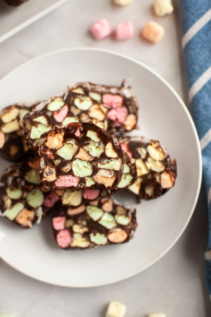 A close-up overhead image of church window cookie slices stacked on a white plate, highlighting the pastel marshmallows and chocolate coating.