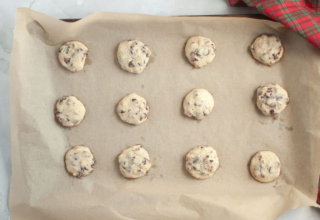 Freshly baked cranberry chocolate chip cookies on a parchment-lined baking sheet, lightly golden around the edges.