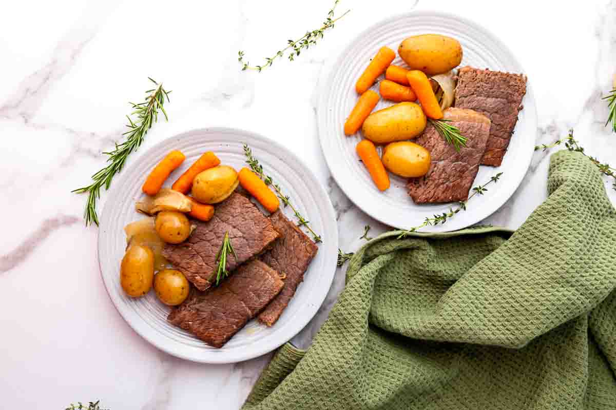 Plates of roast beef and veggies on marble.