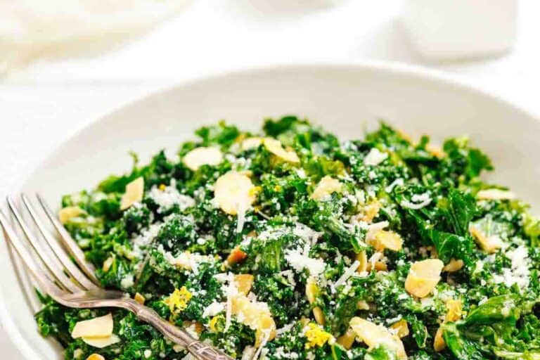 Fresh kale salad with sliced almonds, grated cheese, and lemon zest in a white bowl with a fork.