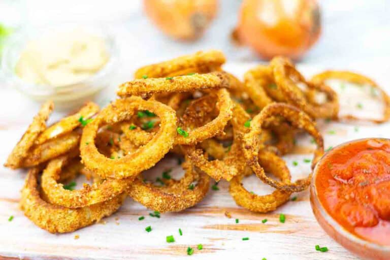 Golden-brown onion rings garnished with chives, served with creamy mustard and tomato-based dipping sauces.