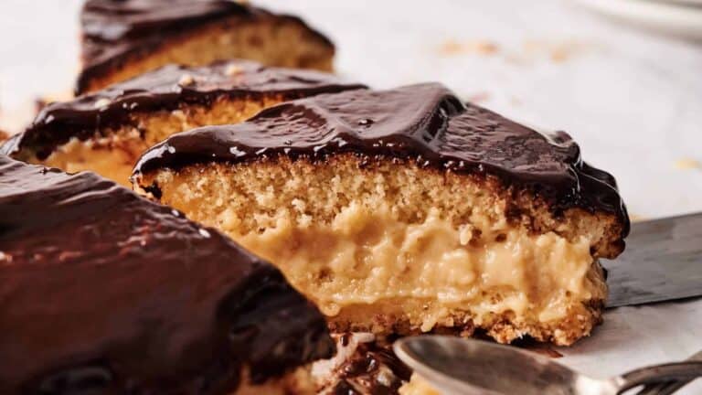 A slice of Boston cream pie showing a thick layer of custard filling inside a spongy cake, topped with glossy chocolate ganache.