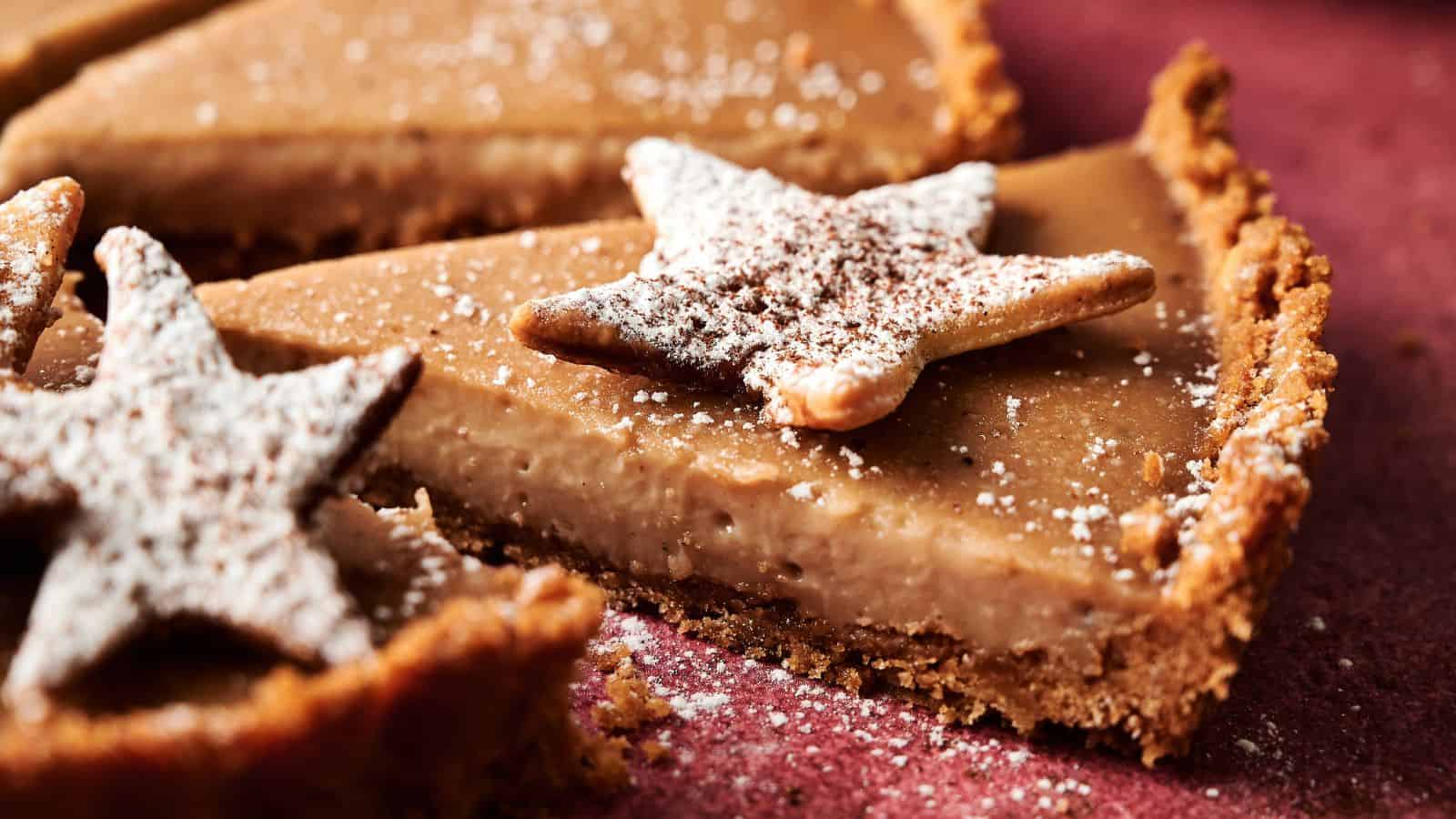 Close-up of a sliced pie with a crumb crust, topped with star-shaped cookies dusted with powdered sugar.