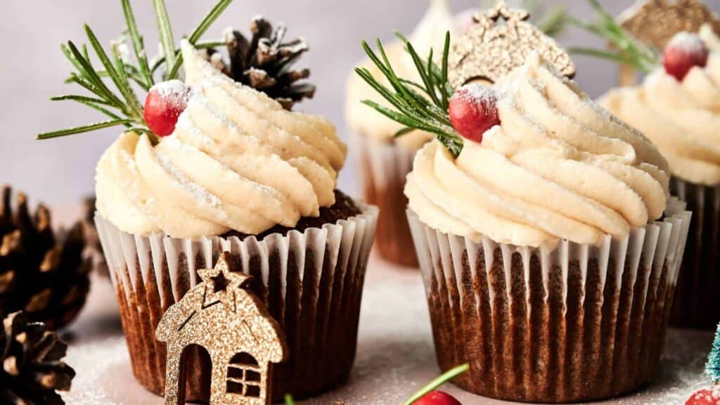 A close-up of gingerbread cupcakes with a swirl of frosting, topped with festive decorations such as gingerbread men and sprinkles.