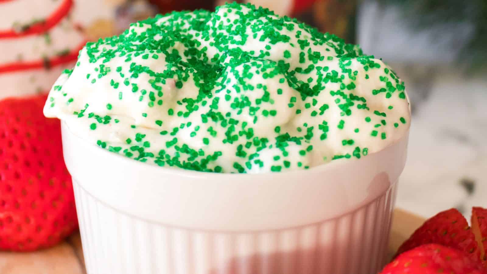 A white bowl filled with whipped cream topped with green sprinkles, surrounded by fresh strawberries.