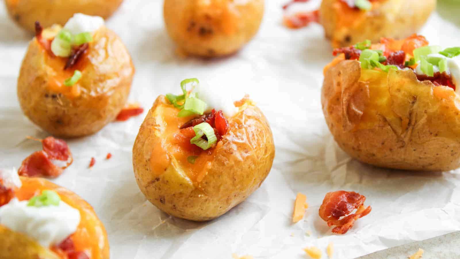 Baked baby potatoes topped with melted cheese, bacon bits, sour cream, and chopped green onions on parchment paper.