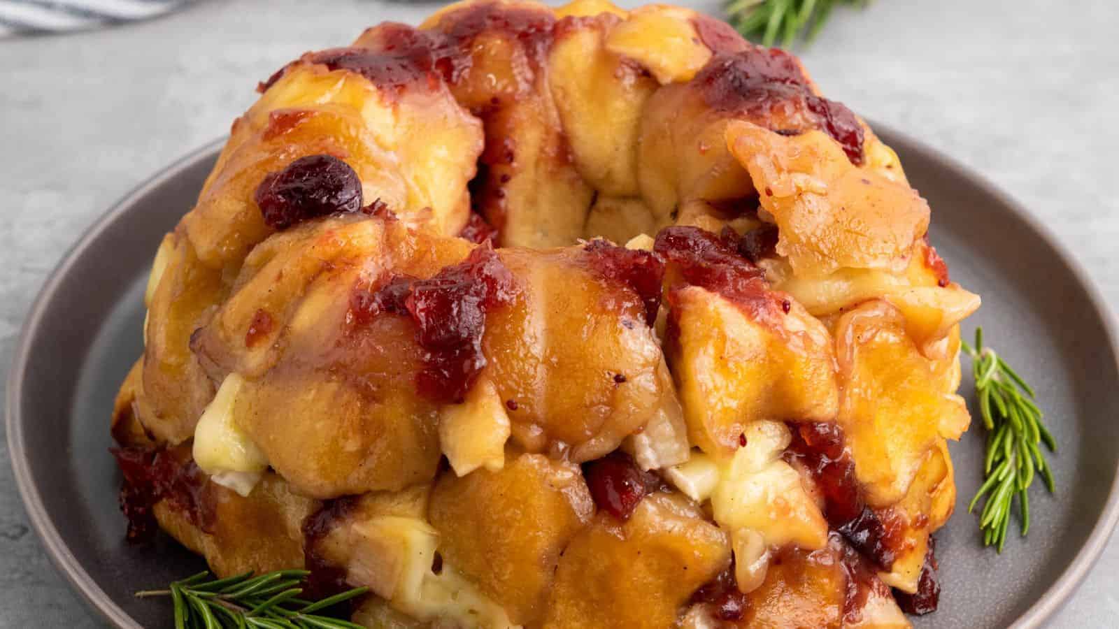 A baked pull-apart bread ring with melted cheese and cranberries on a gray plate, garnished with rosemary sprigs.