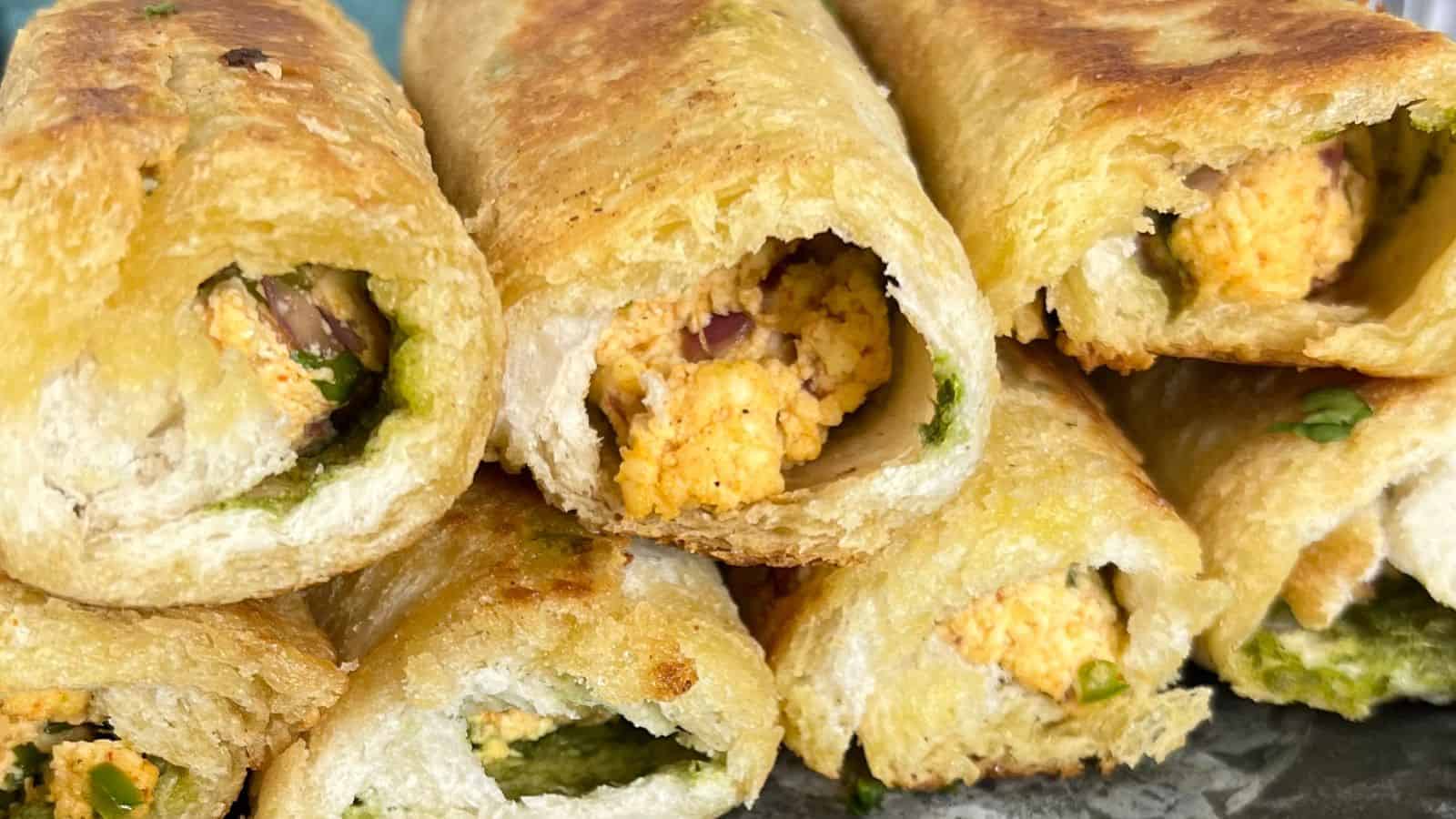 Close-up view of multiple bread rolls stuffed with a mixture of crumbled cheese, onions, and spices, showing crispy golden-brown exteriors and green chutney edges.