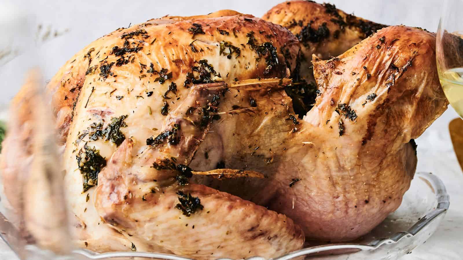 A roasted turkey garnished with herbs, boasting a golden brown, crispy skin, presented on a gleaming glass platter.