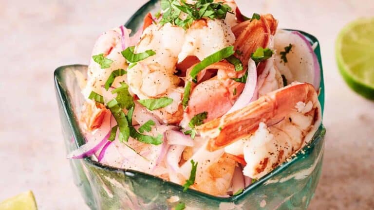 A close-up of shrimp ceviche topped with fresh cilantro and red onion in a glass bowl.