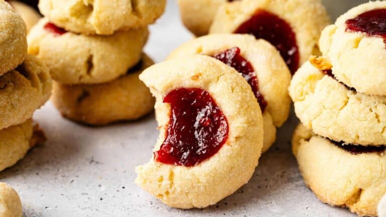 A close-up of thumbprint cookies with a raspberry filling, lightly dusted with powdered sugar.