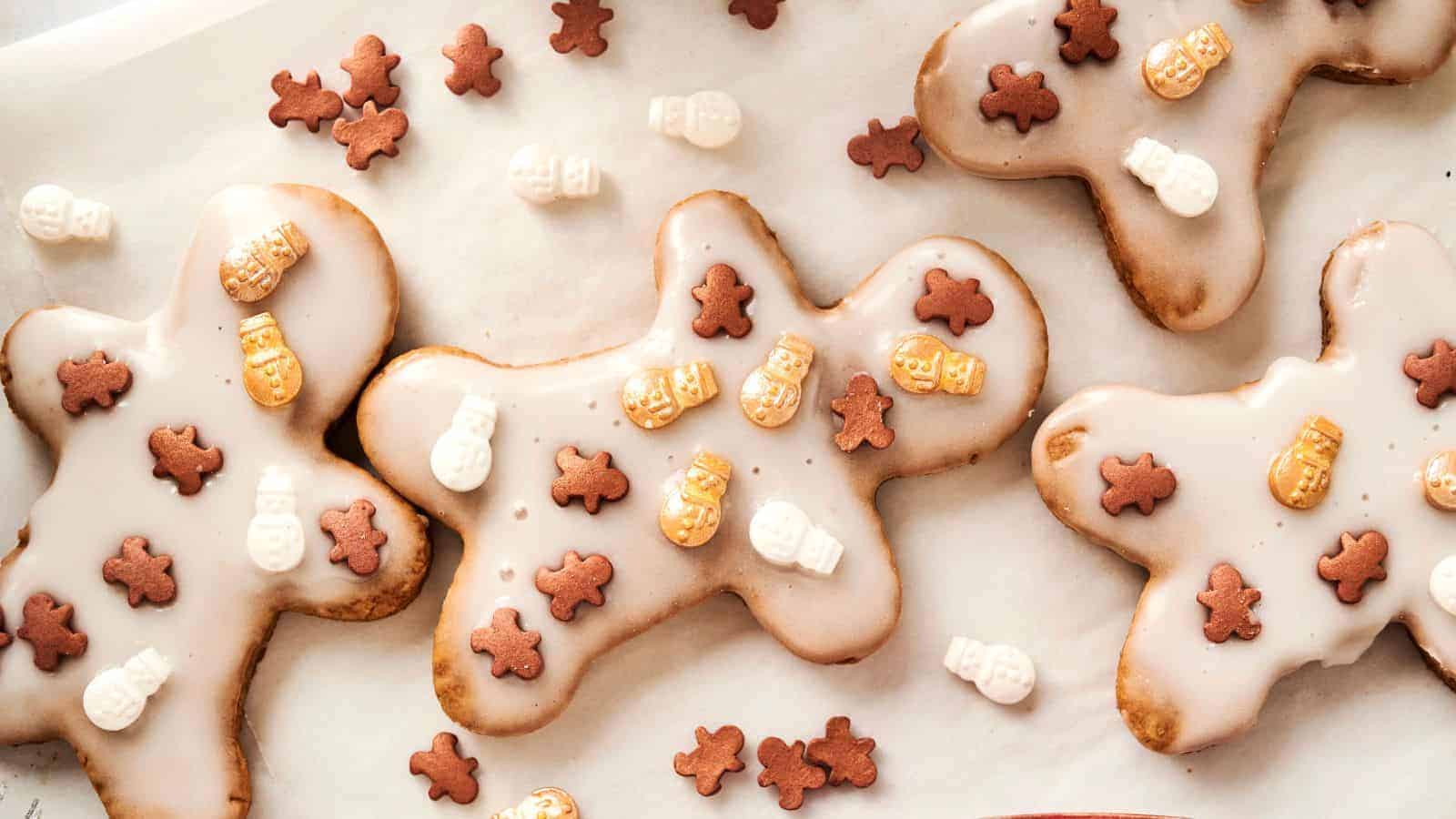 Gingerbread cookies with white icing, topped with small chocolate gingerbread men and snowman decorations, arranged on parchment paper.