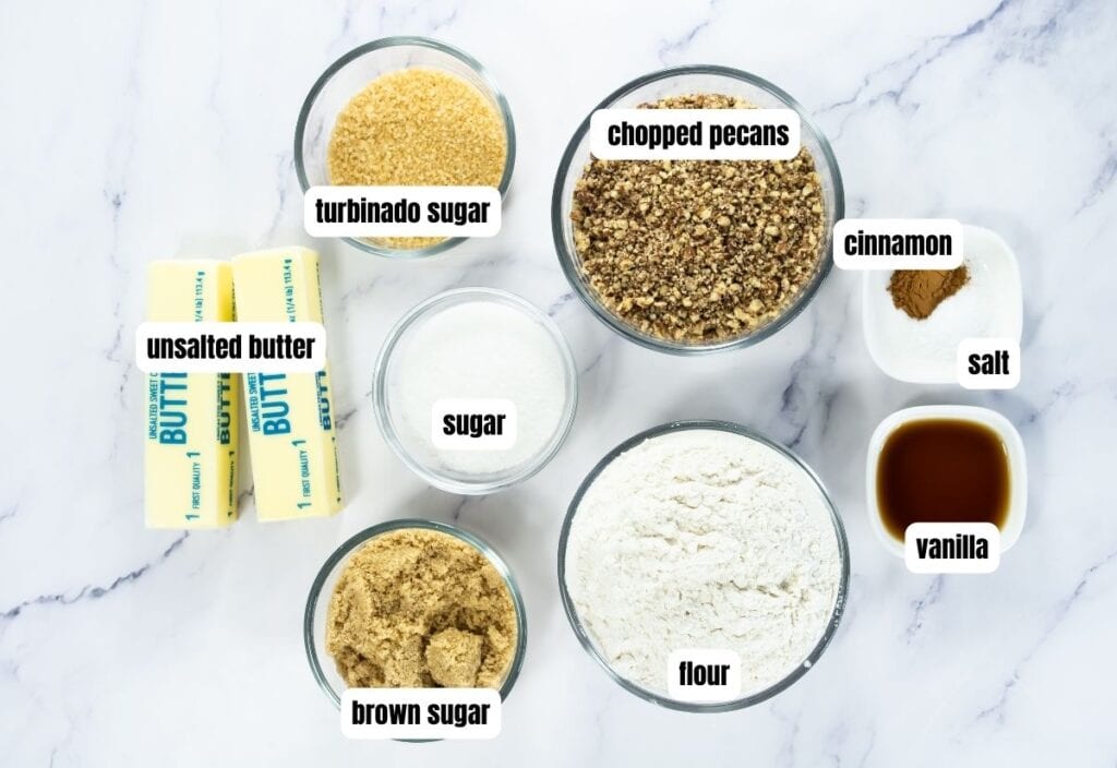 Overhead view of labeled ingredients for pecan shortbread cookies, including butter, sugars, flour, pecans, cinnamon, salt and vanilla.