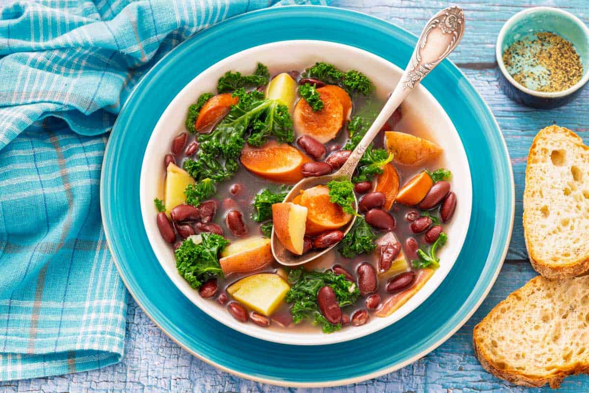 Sausage & Kale Soup in a bowl with carrots, potatoes, and kale, served with a side of bread.