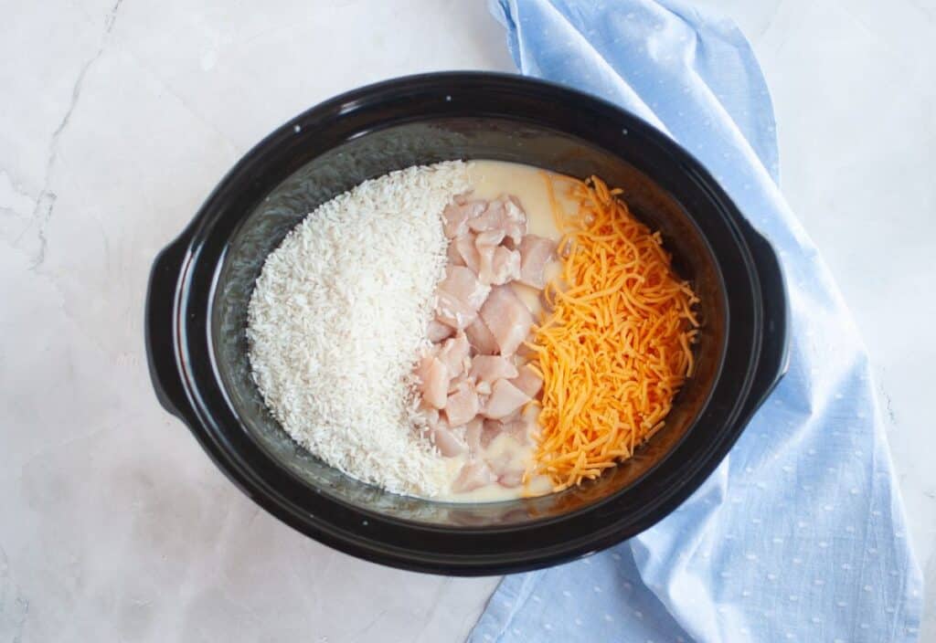 Uncooked rice, raw chicken pieces, and shredded cheddar cheese added to the slow cooker.