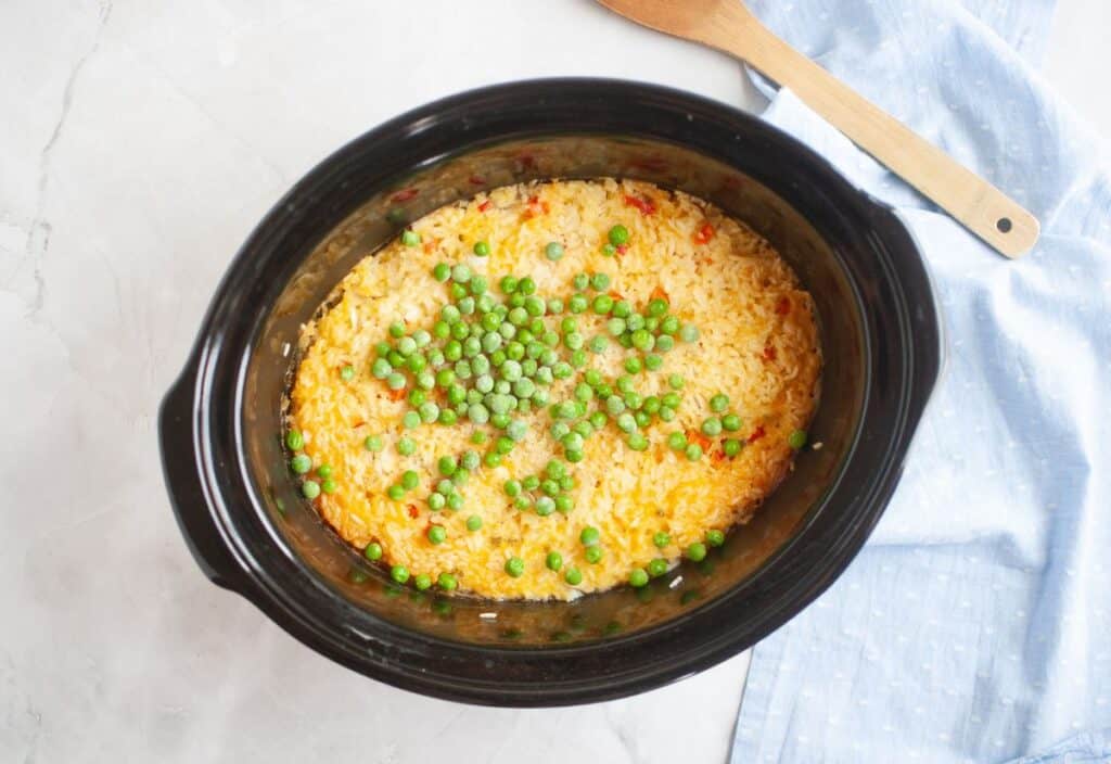 Frozen green peas scattered on top of the cooked chicken and rice.