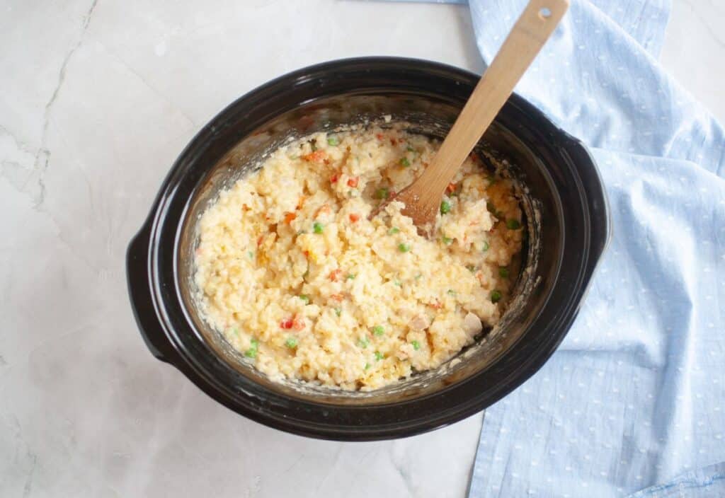 The casserole stirred together, showing peas, peppers, and creamy rice.