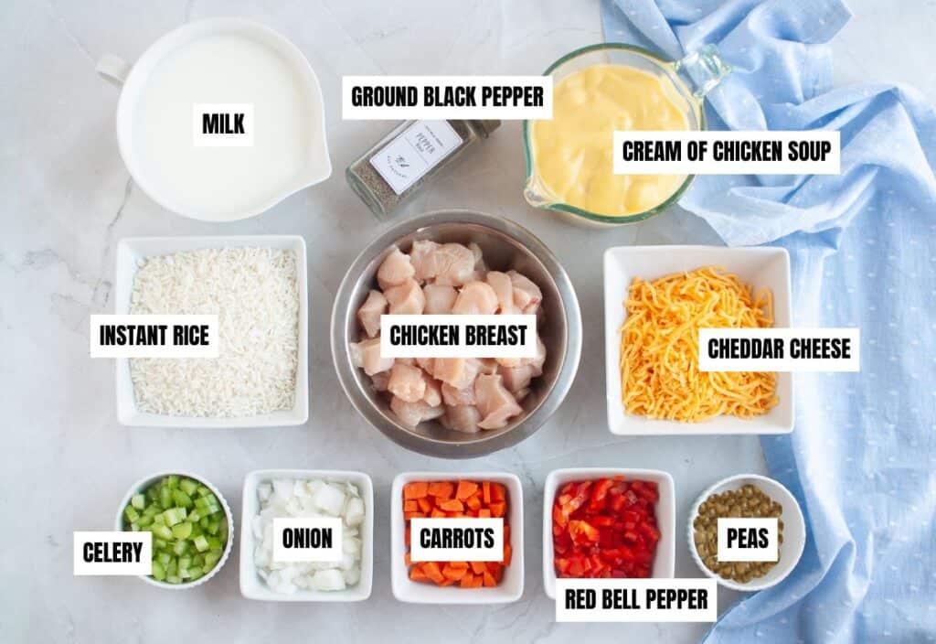 Labeled ingredients for slow cooker chicken and rice arranged on a countertop, including diced vegetables, chicken, rice, cheese, milk, peas, and cream of chicken soup.