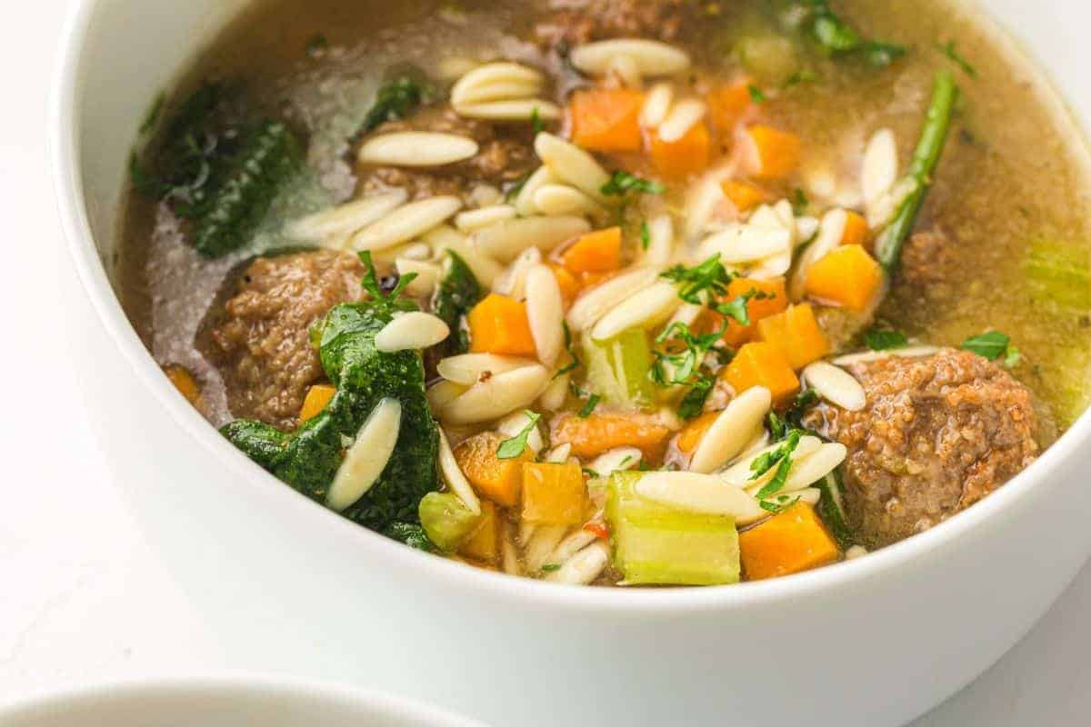 A close-up of a spoon holding a meatball in a bowl of Slow Cooker Italian Wedding Soup.