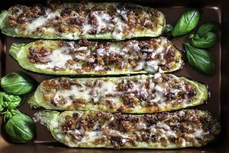 Baked zucchini halves stuffed with savory filling and topped with melted cheese, garnished with fresh basil leaves.