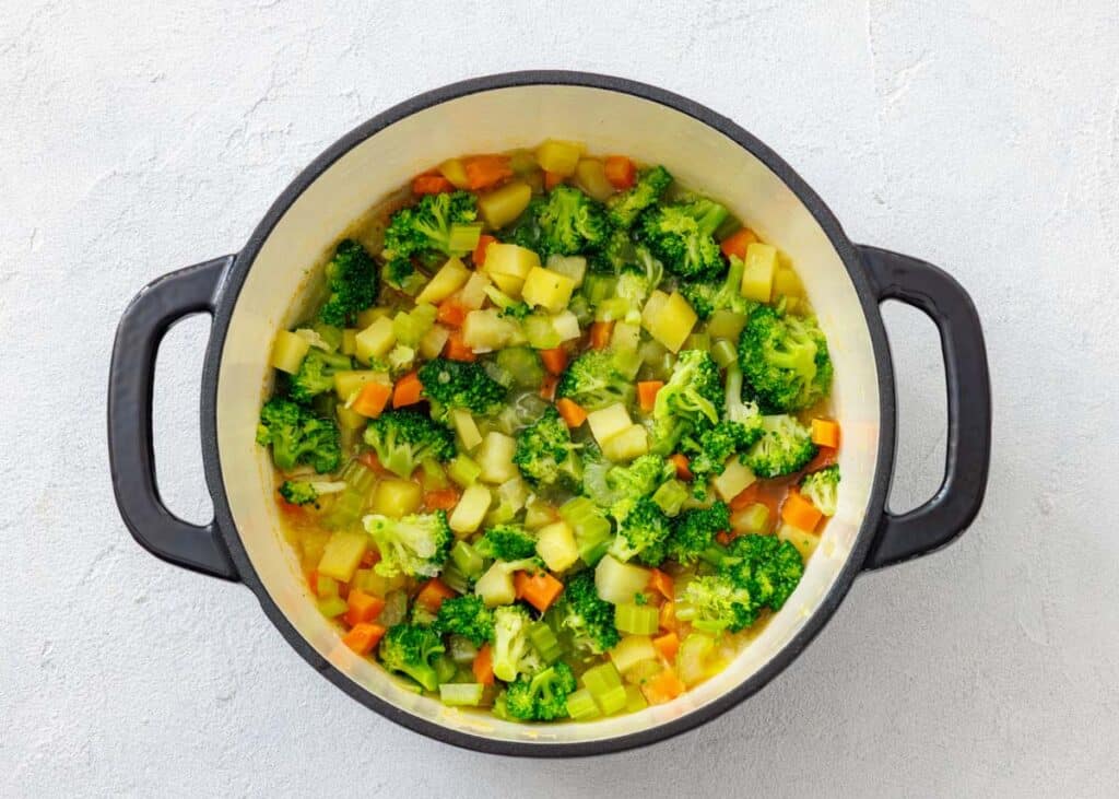A Dutch oven filled with simmering vegetables like broccoli, carrots, and potatoes for the chowder.
