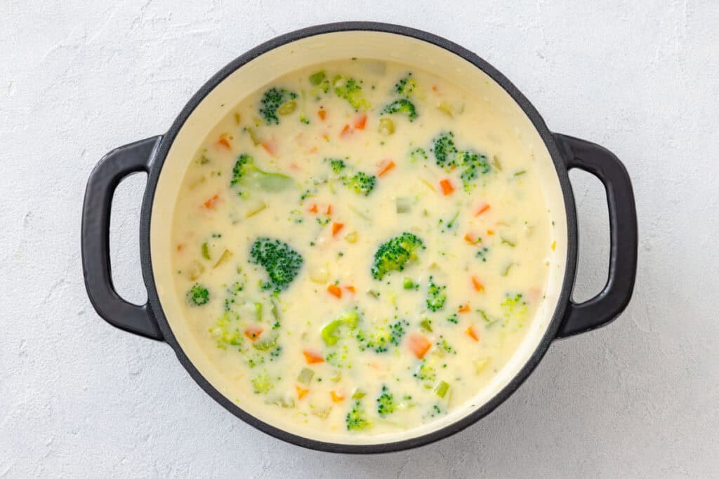 A close-up of creamy vegetable chowder with tender vegetables like broccoli, carrots, and celery in a pot.