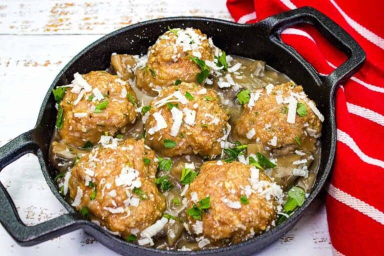 Hearty and tender meatballs served with a savory onion gravy in a cast iron skillet, garnished with fresh parsley and cheese.