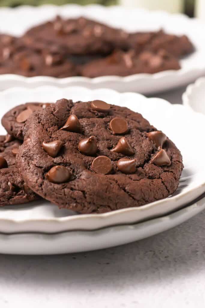 Close-up of baked chocolate cookies stacked on a white plate with visible chocolate chips.