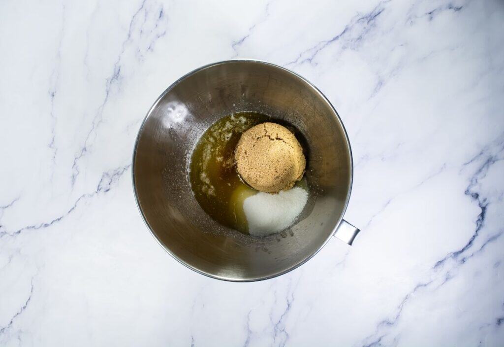 Brown sugar and white sugar are added to the melted browned butter in a mixing bowl, ready to be mixed.