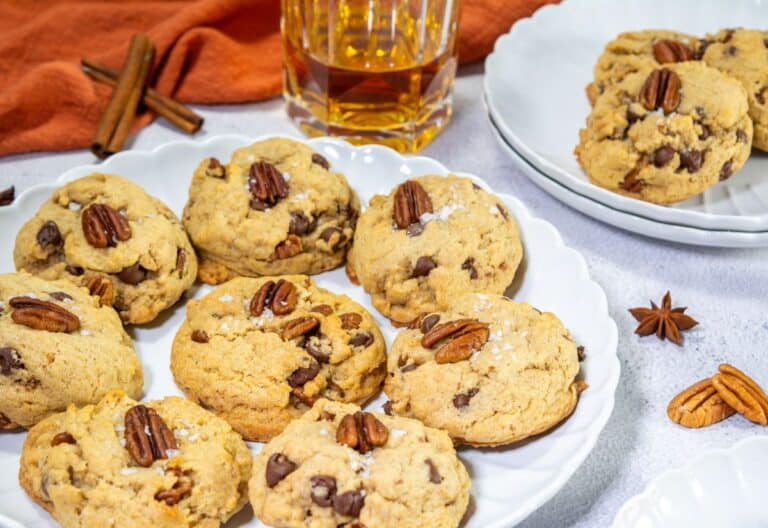 A close-up view of browned butter bourbon pecan chocolate chip cookies with a pecan on top, sprinkled with flaky sea salt.