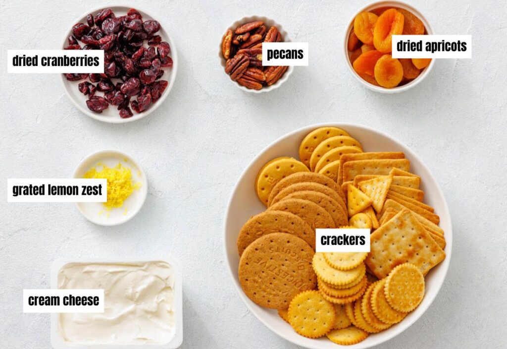 The ingredients for cranberry dip, including dried cranberries, apricots, pecans, grated lemon zest, cream cheese, and crackers, neatly arranged in bowls.