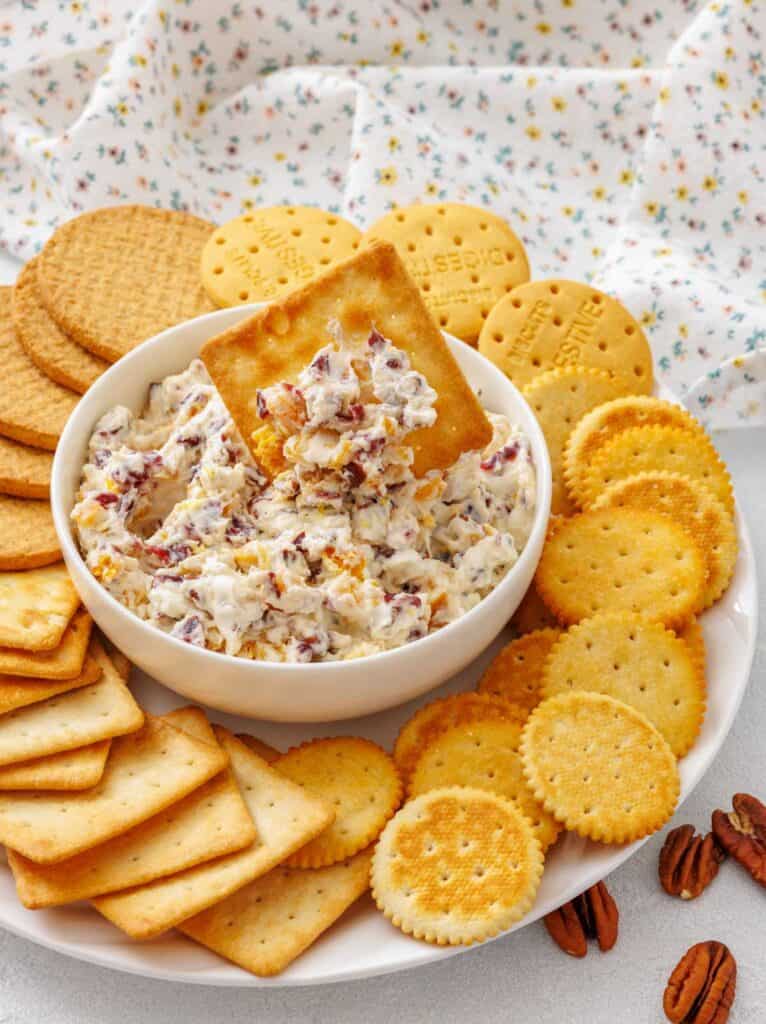 A close-up of cranberry dip served in a white bowl surrounded by crackers, with a portion of the dip scooped onto a cracker.