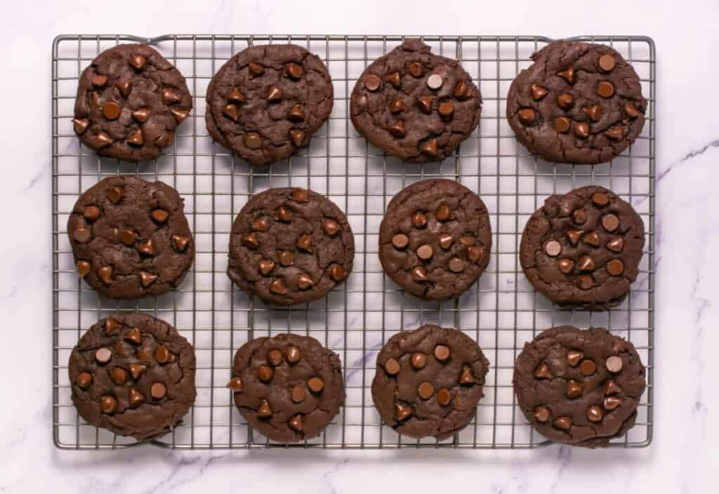 Freshly baked chocolate cookies cooling on a wire rack, topped with melted chocolate chips.