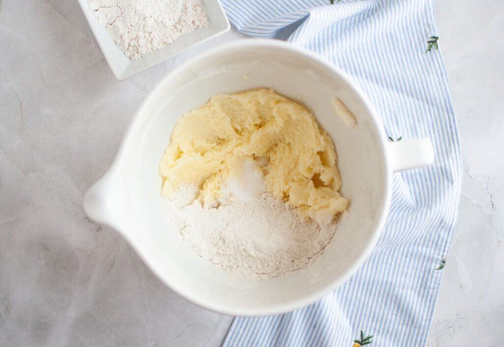 bowl with creamed butter and sugar mixture, with flour added on top, ready to be mixed.