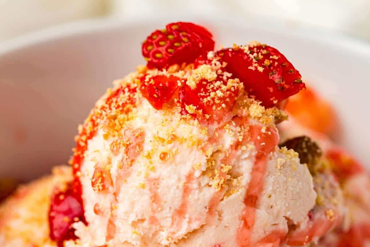 Close-up of a bowl of ice cream topped with crushed cookies, strawberry pieces, and a drizzle of strawberry sauce.