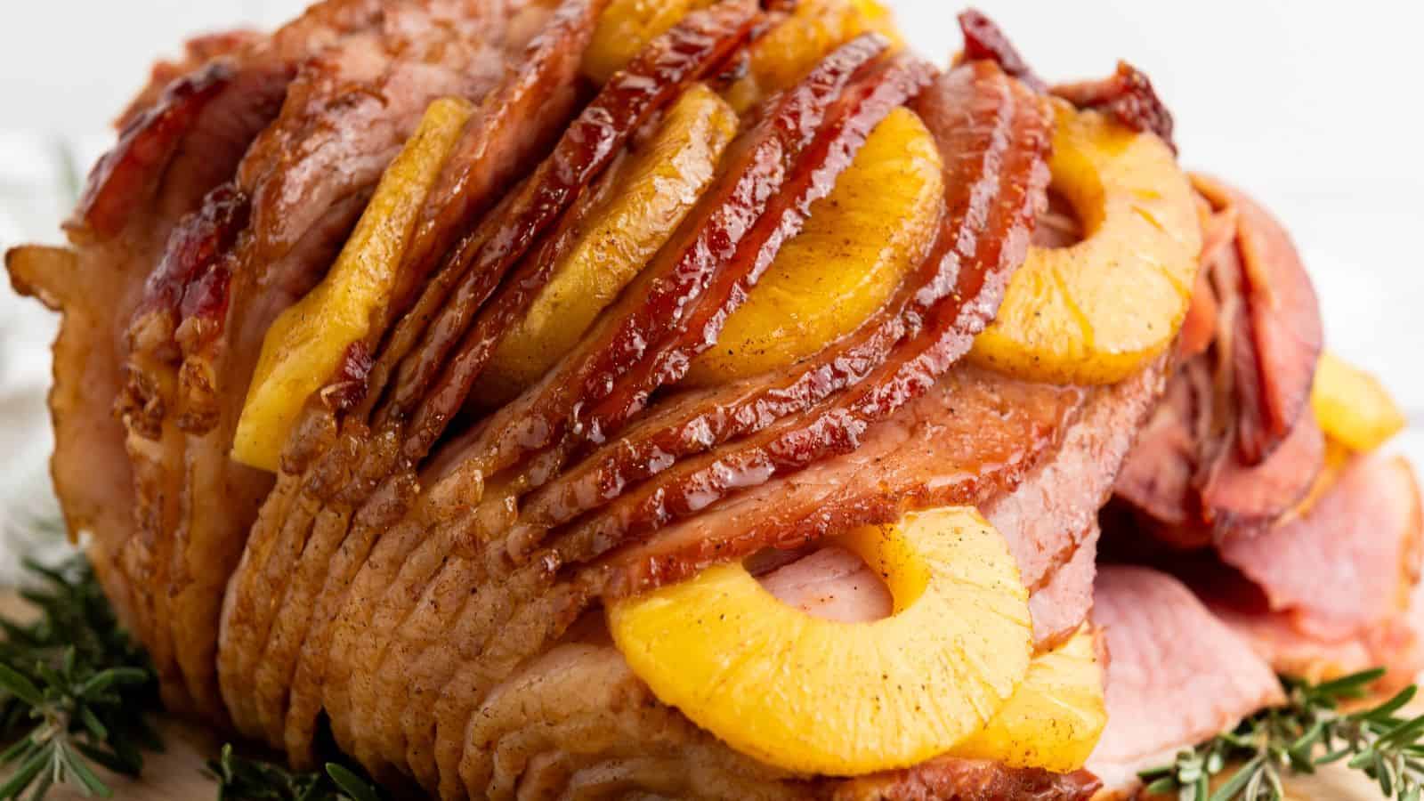A Brown Sugar Pineapple Ham is placed on a wooden board, garnished with sprigs of rosemary.