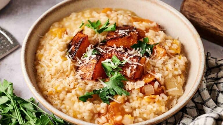 A creamy bowl of butternut squash risotto, topped with roasted squash cubes and a sprinkle of Parmesan cheese.