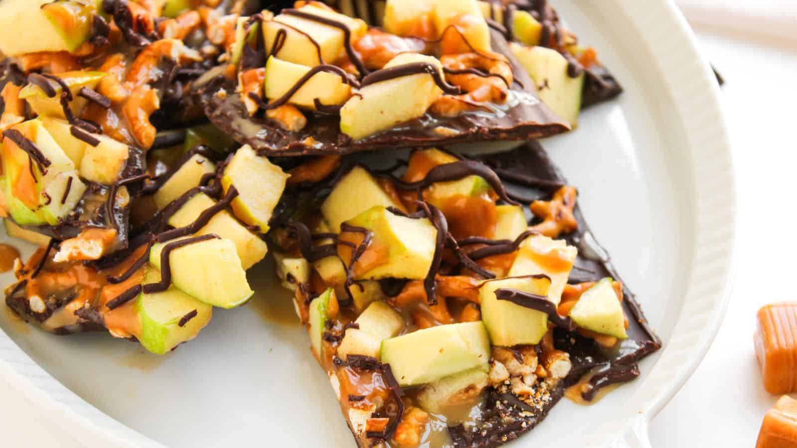 A plate of caramel apple bark, featuring chocolate, caramel, and apple chunks, with drizzled chocolate on top.