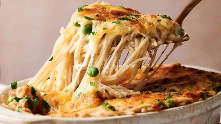 A casserole dish filled with creamy chicken tetrazzini pasta, with visible spinach and a golden, melted cheese topping.