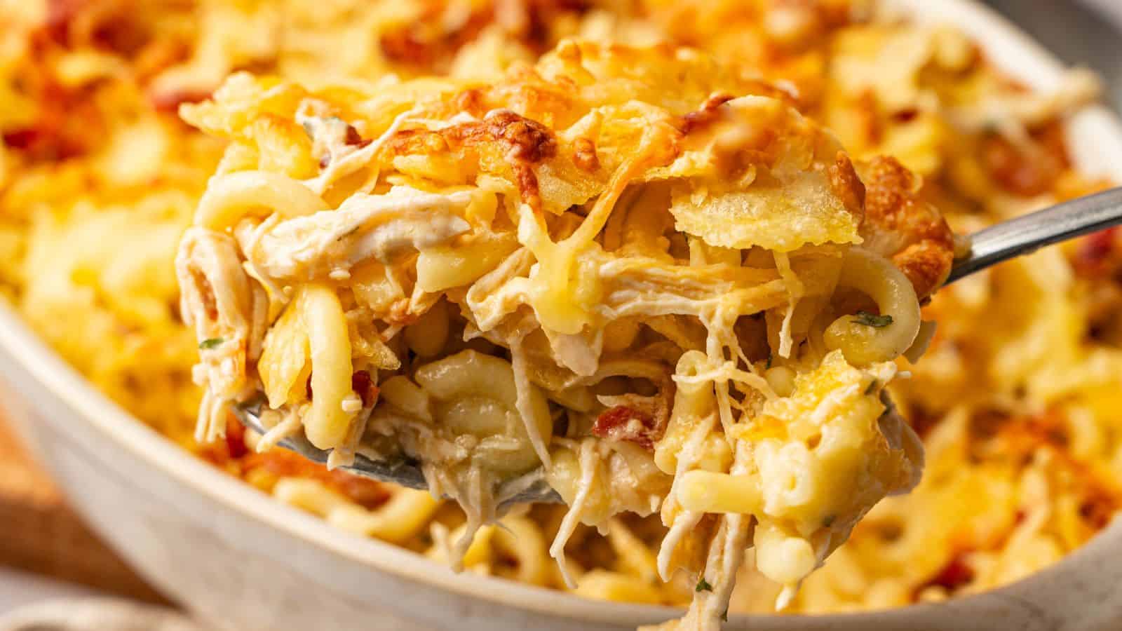 A fork lifting a cheesy bite from a bowl of chicken casserole topped with bacon and breadcrumbs.