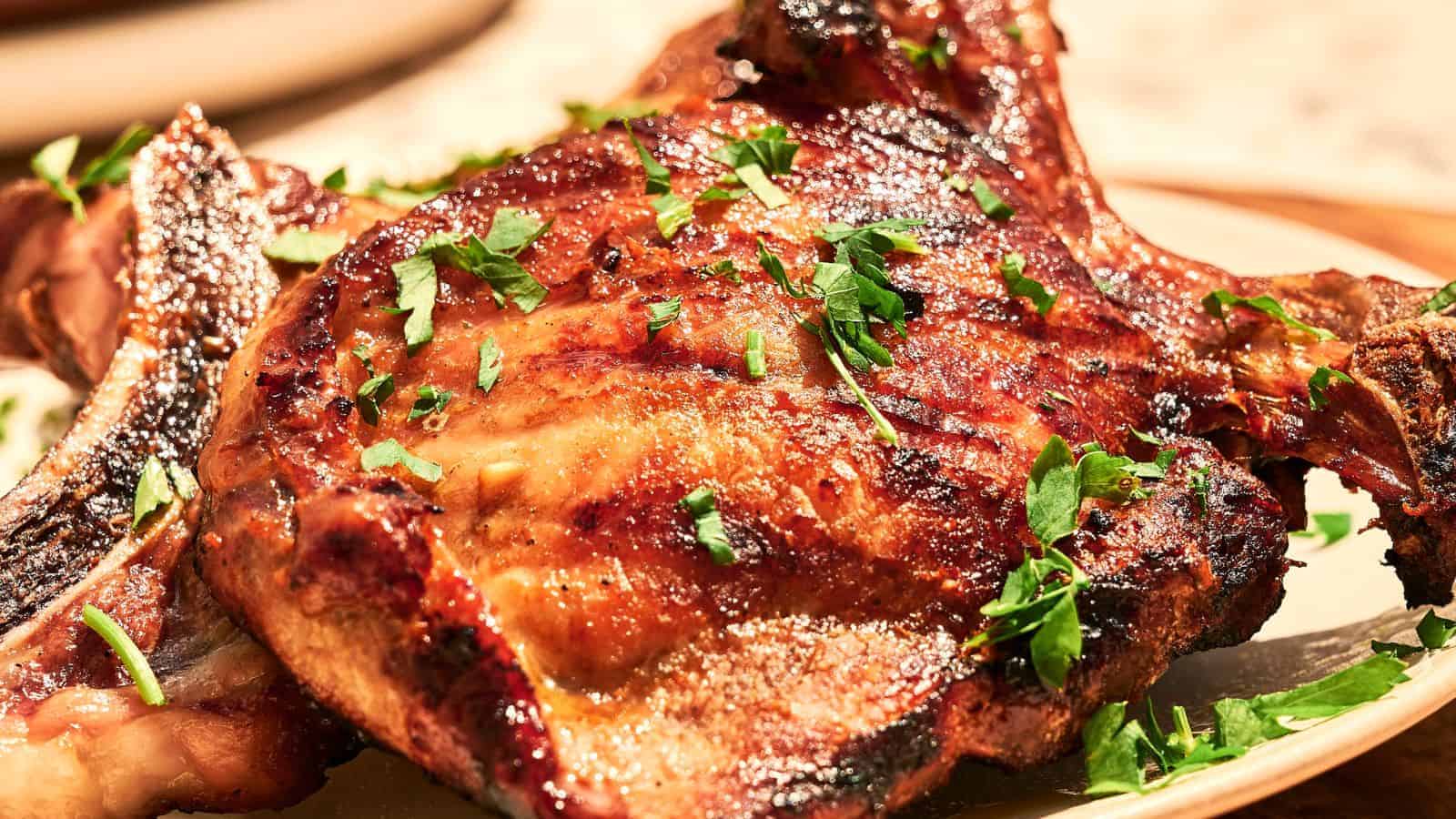 Close-up of a cooked, seasoned pork chop topped with melted cheese and garnished with chopped parsley on a dark plate.
