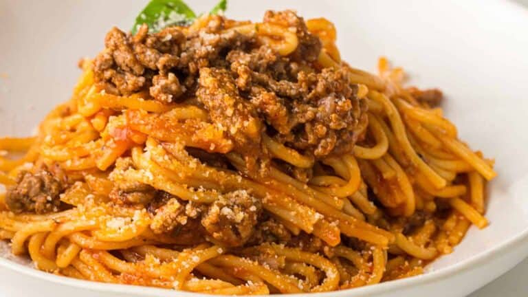 Spaghetti noodles topped with beef bolognese sauce, served in a white bowl with grated parmesan and garnished with basil.