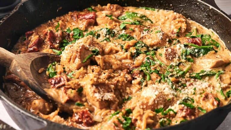 A dish of orzo pasta served with marry me chicken, cooked in a rich, creamy sauce with sun-dried tomatoes and spinach.
